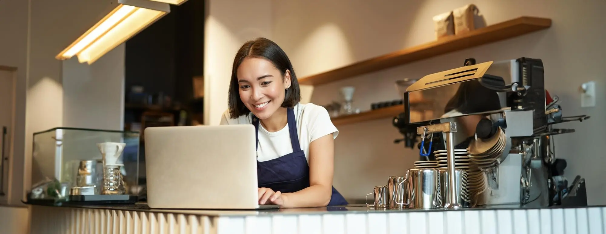 Porträt eines lächelnden asiatischen Baristas, Caféinhabers und Unternehmers, der am Laptop arbeitet und Bestellungen bearbeitet, auf